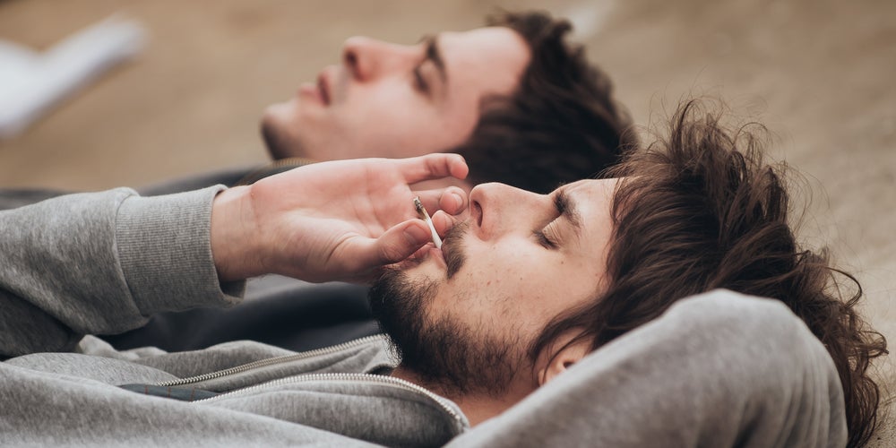 2 young men lying down and smoking a joint on the beach.