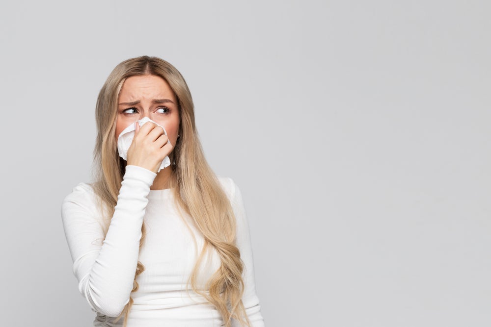 Woman allergic to weed. She has a runny nose that she is holding with a white handkerchief.