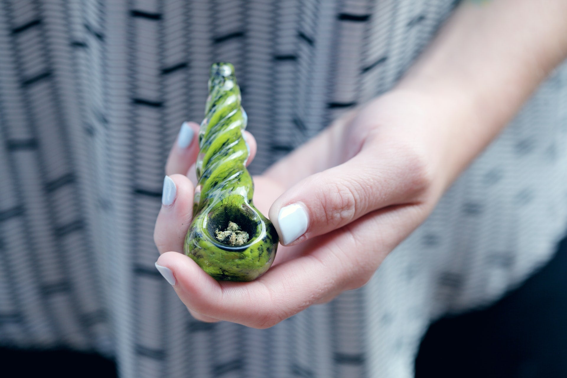 A bowl of cannabis in a pipe. A girl is holding the pipe in her left hand.