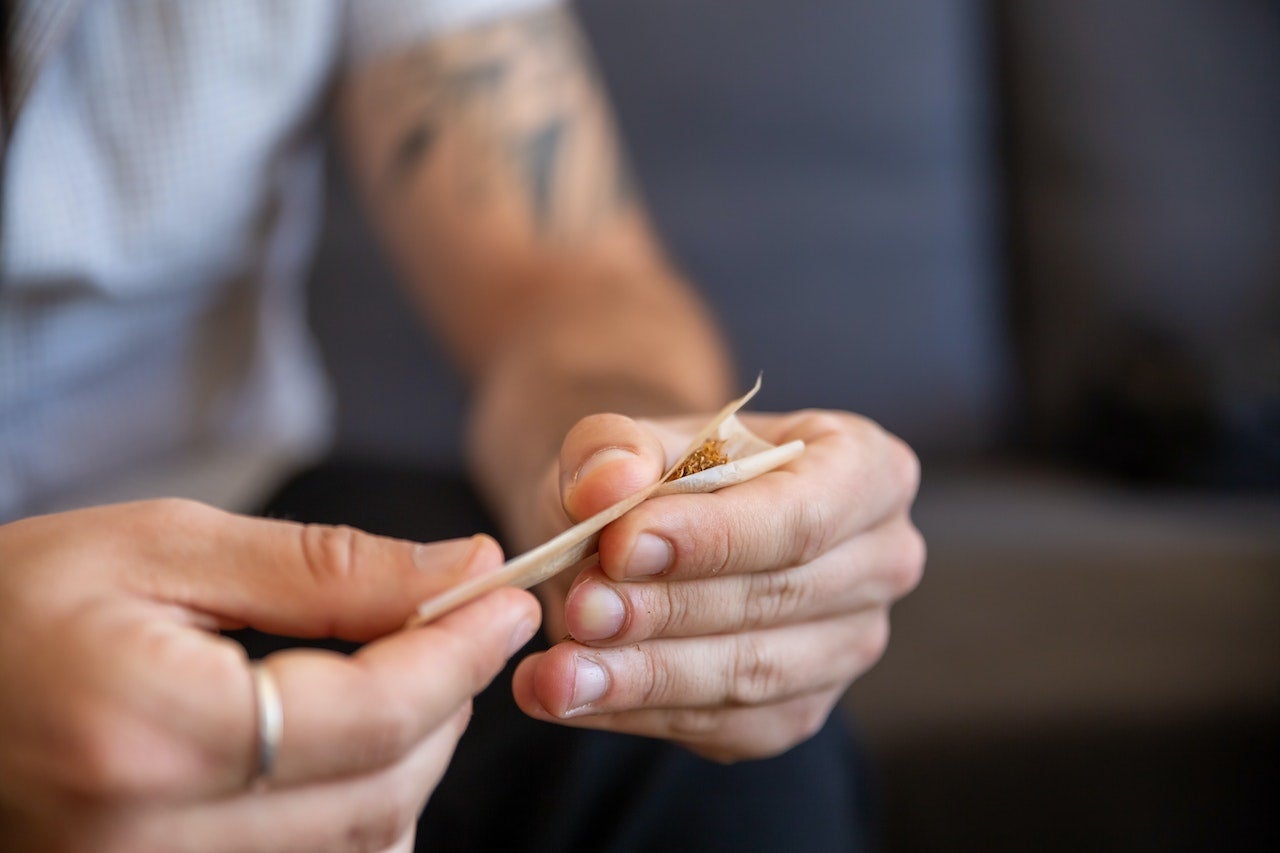 Young male holding rolling paper with cannabis flower. He is holding each side with each of his hands.